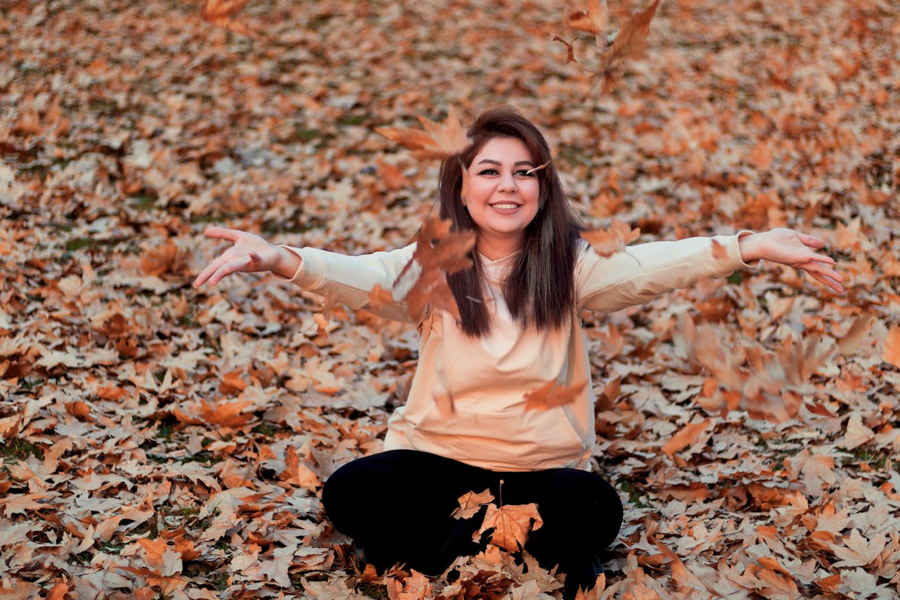 Smiling woman with arms outstretched enjoying autumn leaves outdoors in Tehran.