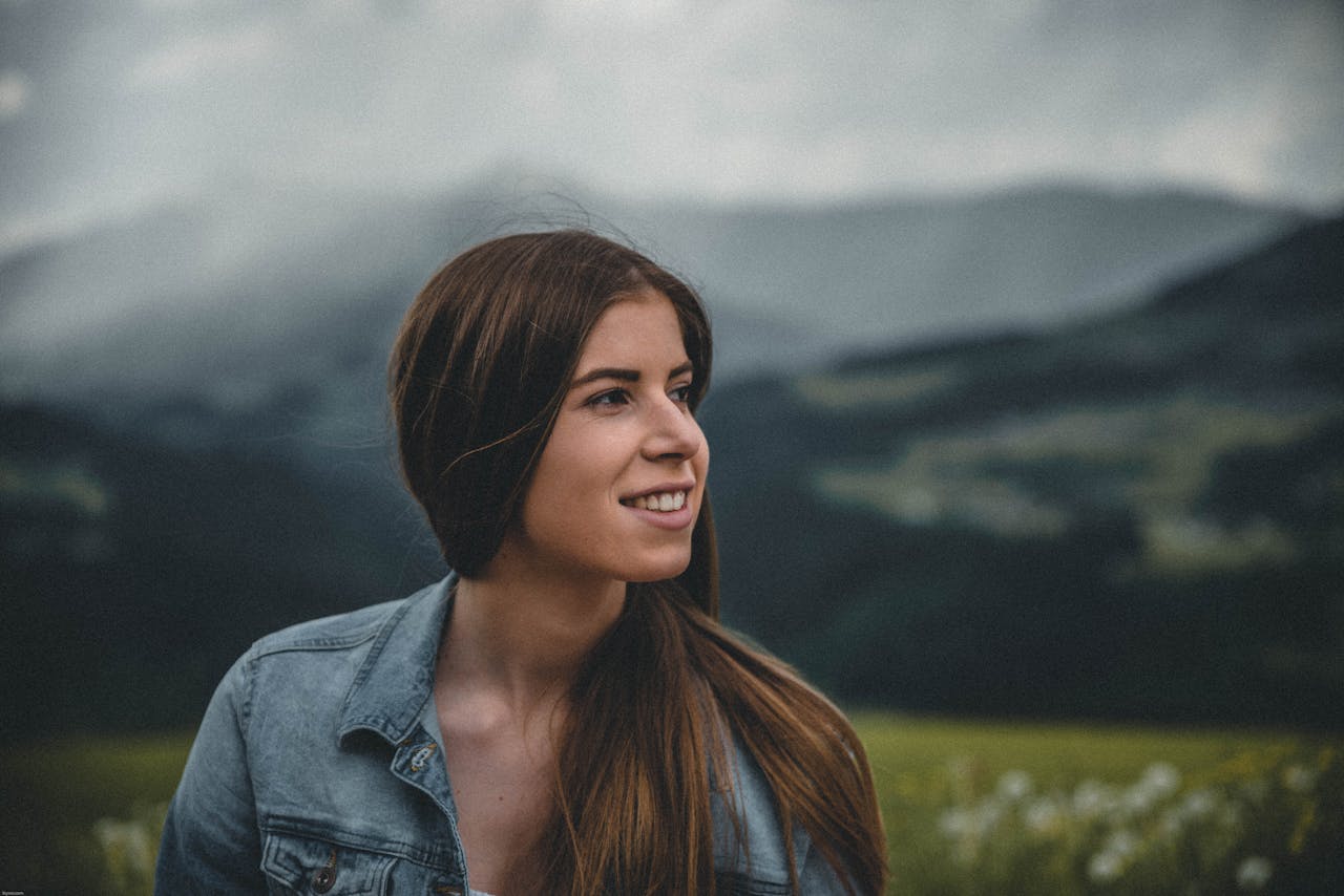 Smiling woman in a denim jacket with mountains in the background in Kitzbühel, Austria.