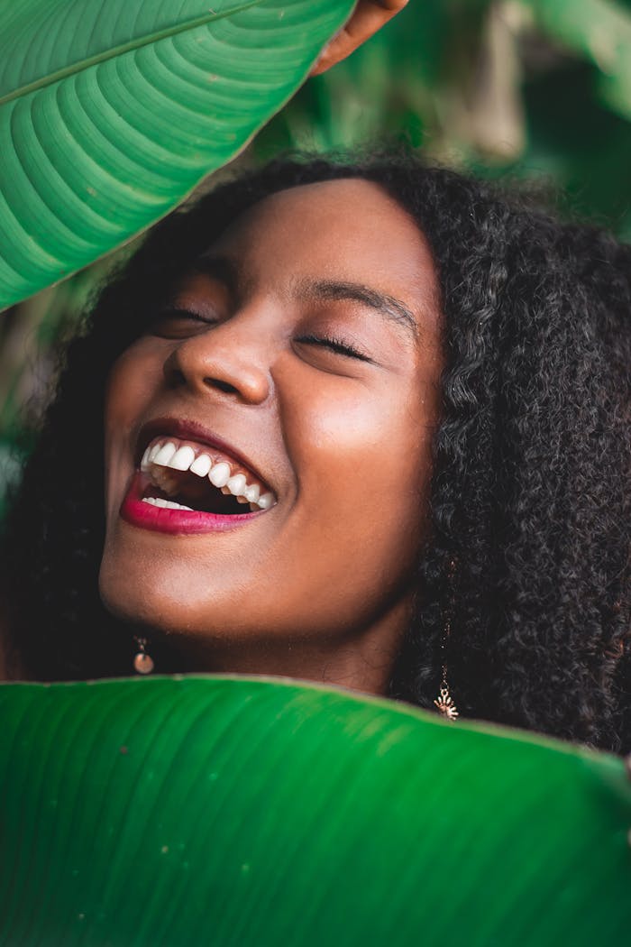 A vibrant portrait of a woman laughing joyfully surrounded by lush green leaves.