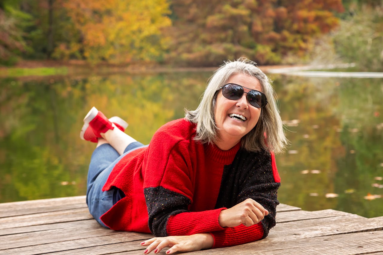 A woman enjoying a relaxing day by a pond in autumn, with vibrant fall foliage and a joyful smile.