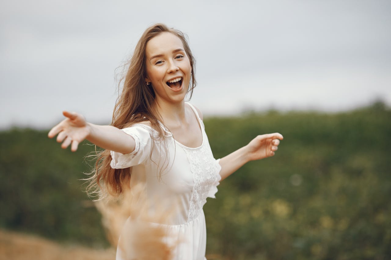 Smiling woman in a white dress enjoying nature with open arms.